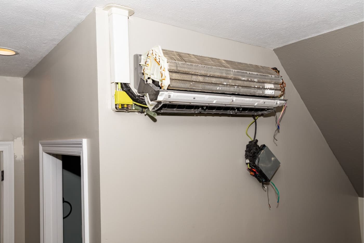 A broken air conditioner is hanging on a wall next to a door