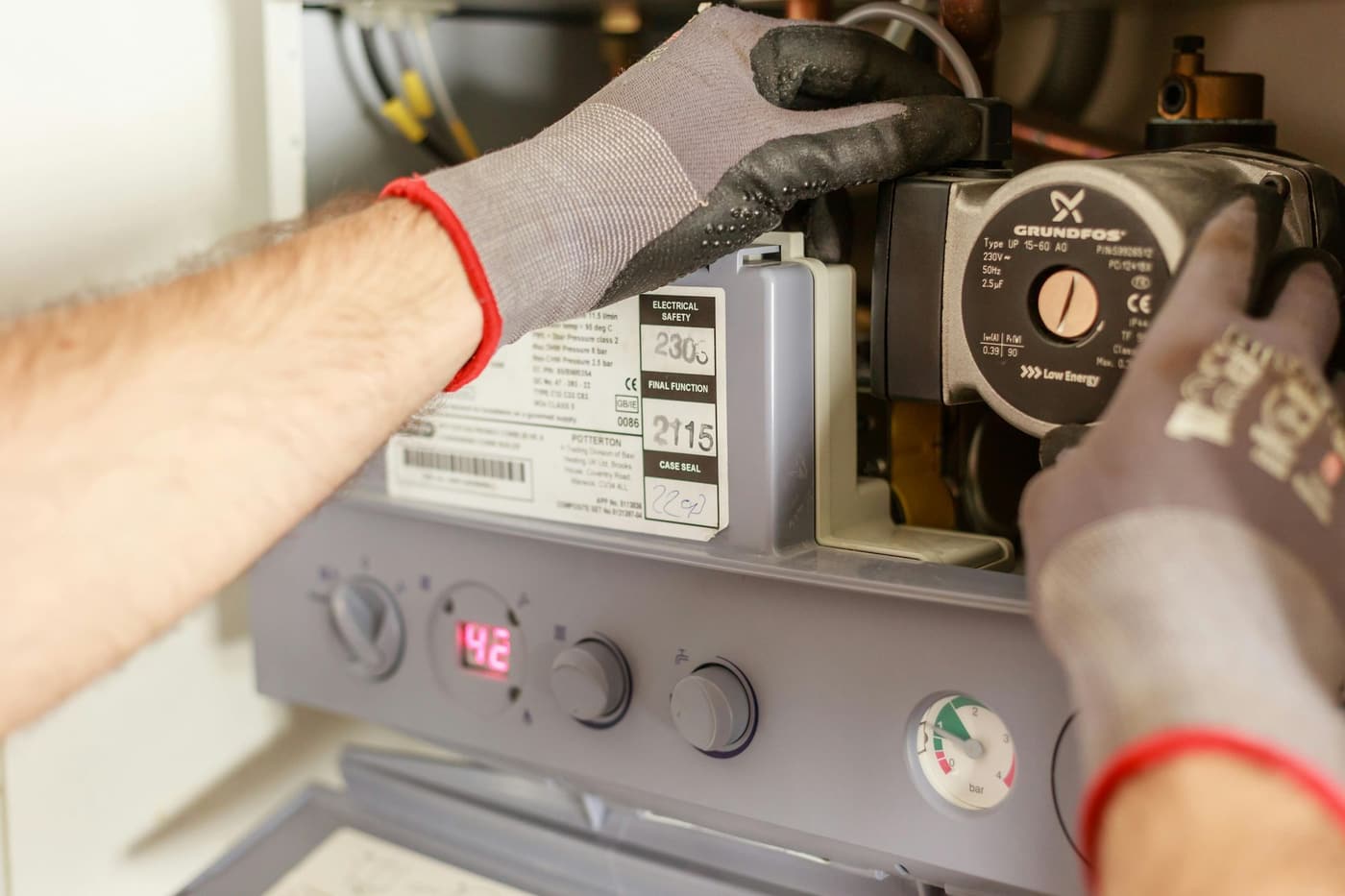 Gloved hands adjusting a boiler's control knob and wiring panel