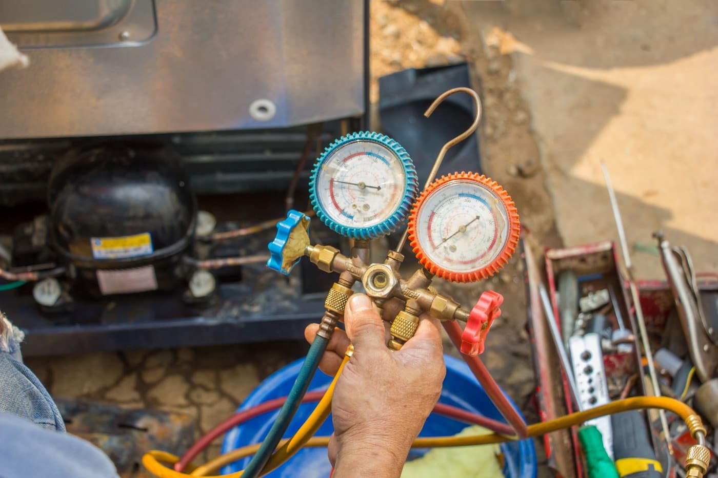 Technician holding refrigerant manifold gauges over a refrigeration compressor