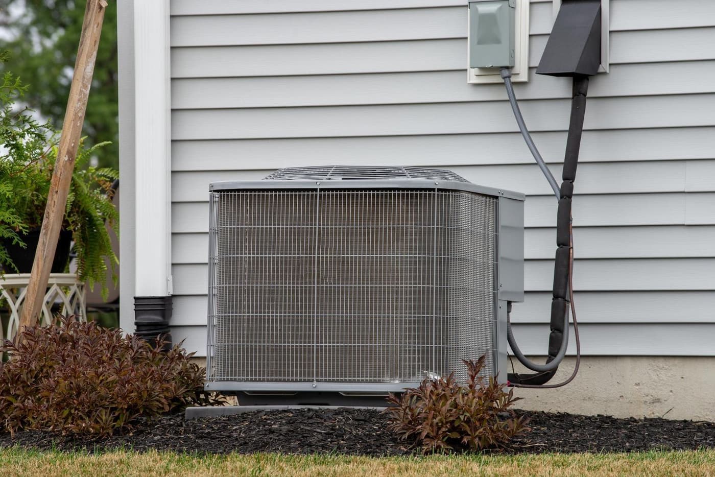 Central air conditioner condenser on a pad beside a house with gray lap siding