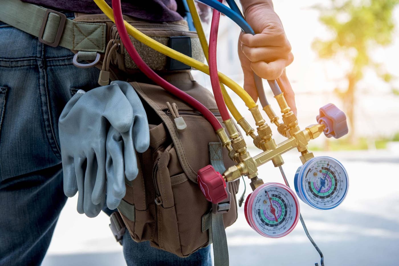 HVAC technician with a tool belt holding refrigerant gauges and hoses